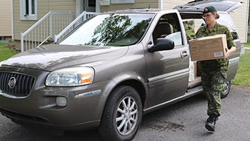 A military member is moving a box out of a mini van.